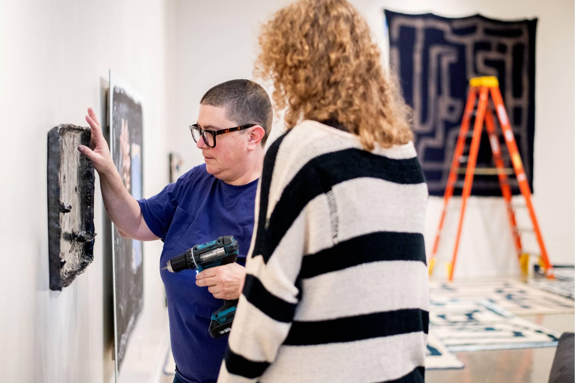 Students working to hang an image-based ceramic artwork with guest artist Emmy Bright.